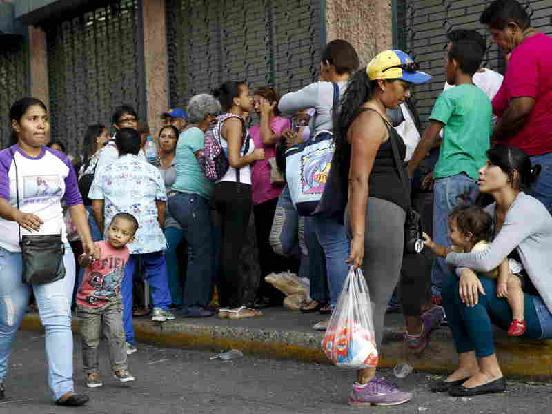 Mothers take care of their children while lining up to buy staple goods outside a supermarket in Caracas earlier this month.